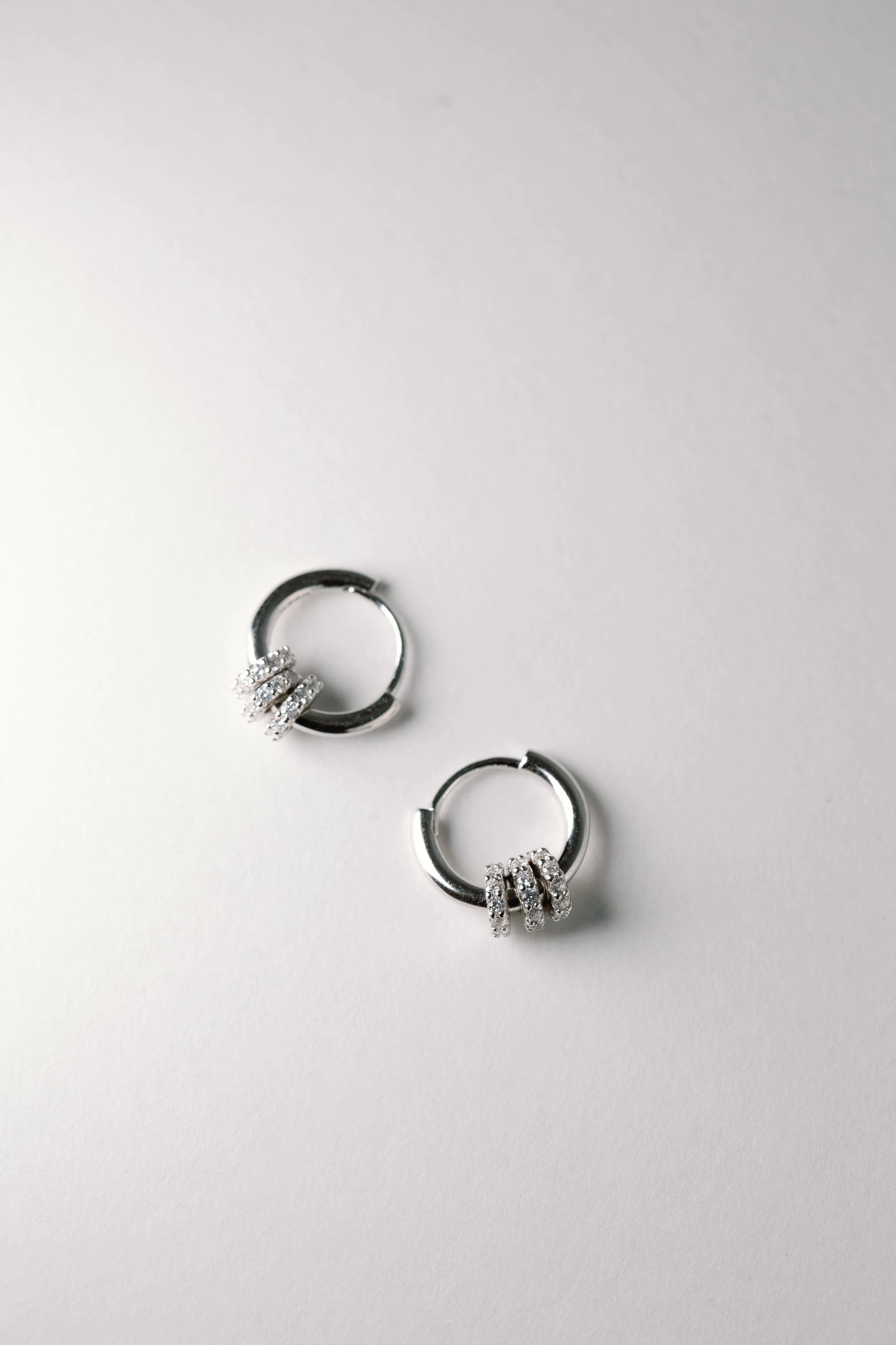 Knot huggie earrings pair flat-lay, silver hoops each tied with a crystal-pave wrapped knot