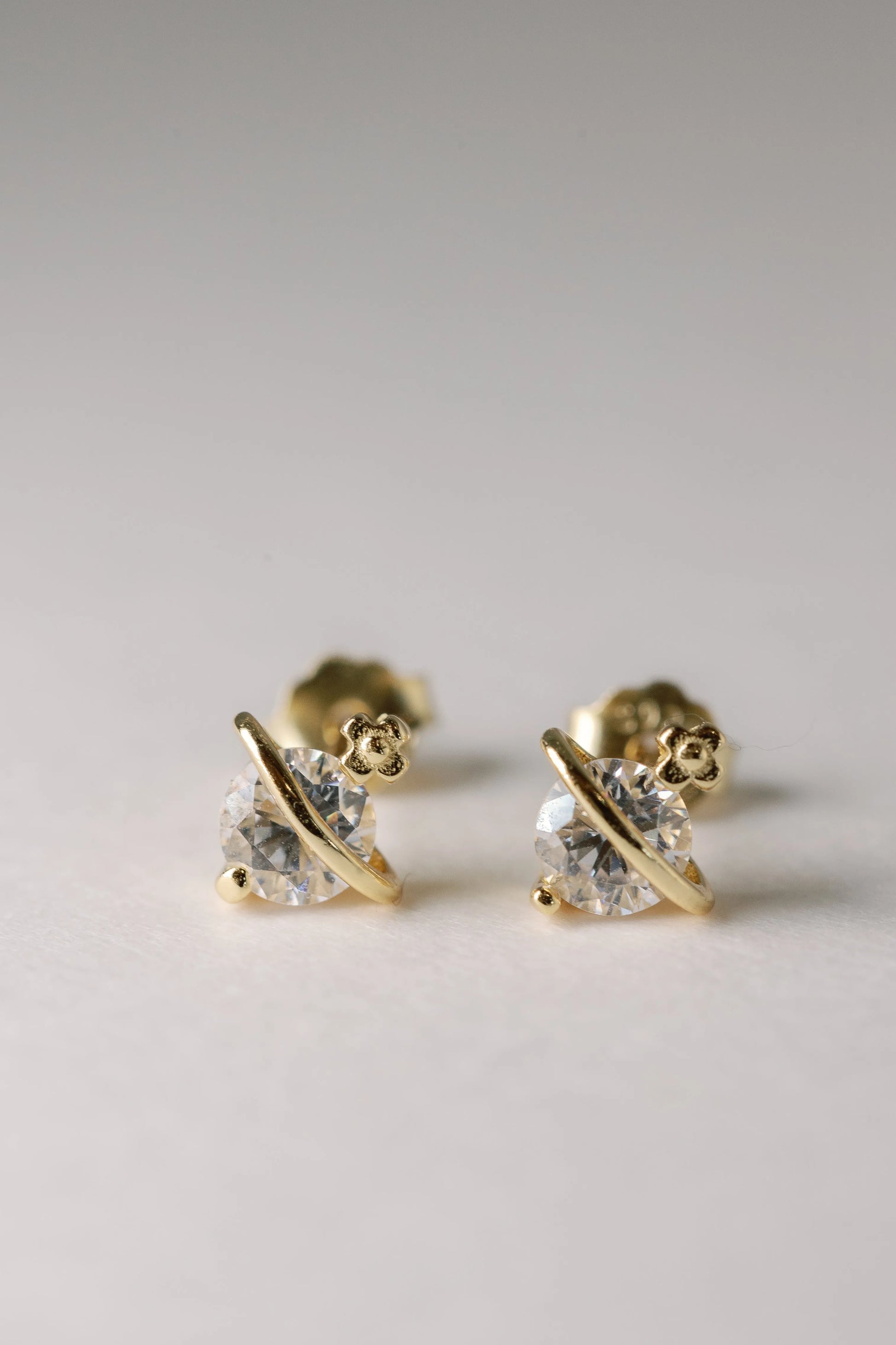 Gold Astro Crystal studs with clear crystals and saturn-ring bands, close-up against a pale backdrop