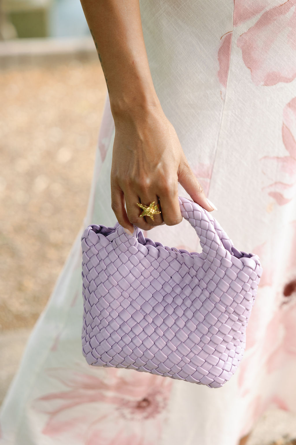 Person holding a purple woven handbag with a blurred floral background