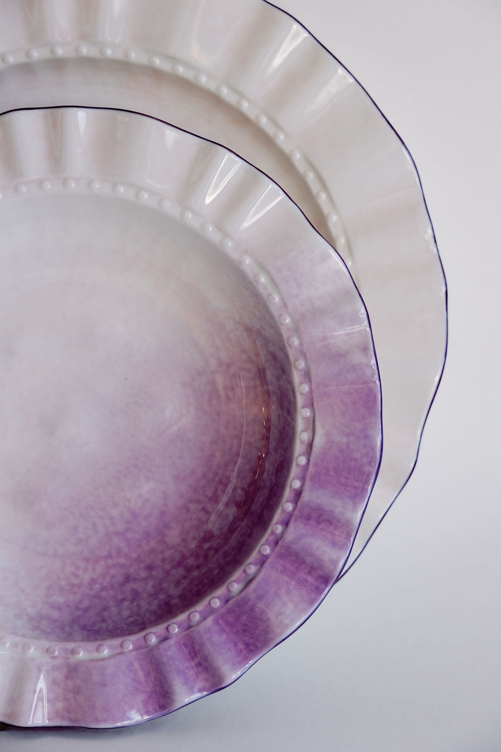Close-up of lavender ombre ruffle pasta plates, beaded scalloped rims fading from purple to white.