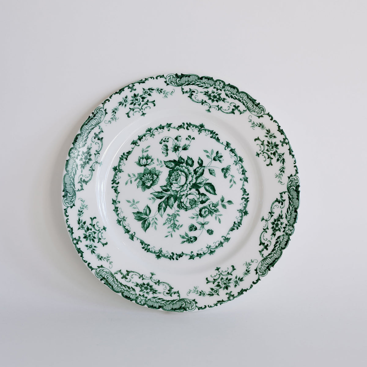 A white ceramic plate with a green floral toile pattern, photographed from directly above against a clean white background.