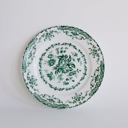 A white ceramic plate with a green floral toile pattern, photographed from directly above against a clean white background.