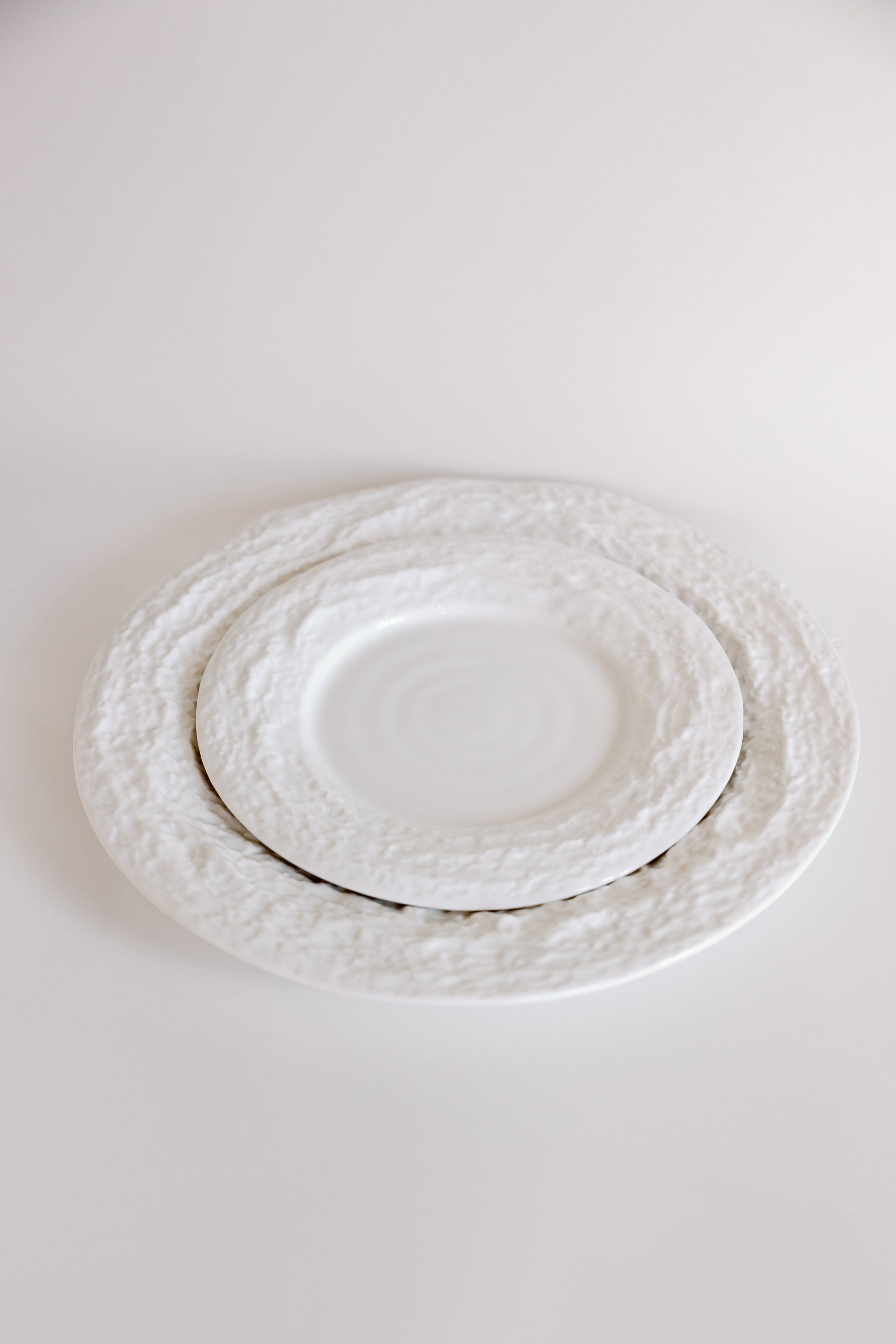 White Alpine Snow porcelain plates with craggy textured borders shown at an angle, smaller plate nested on larger.