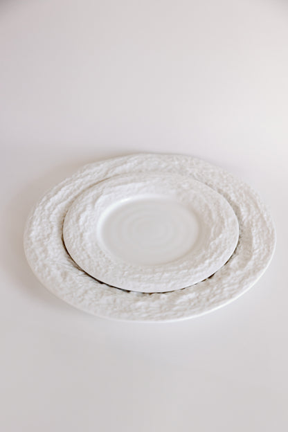 White Alpine Snow porcelain plates with craggy textured borders shown at an angle, smaller plate nested on larger.