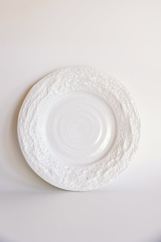 White Alpine Snow porcelain dinner plate with textured crackled rim and swirled center on a pale background.