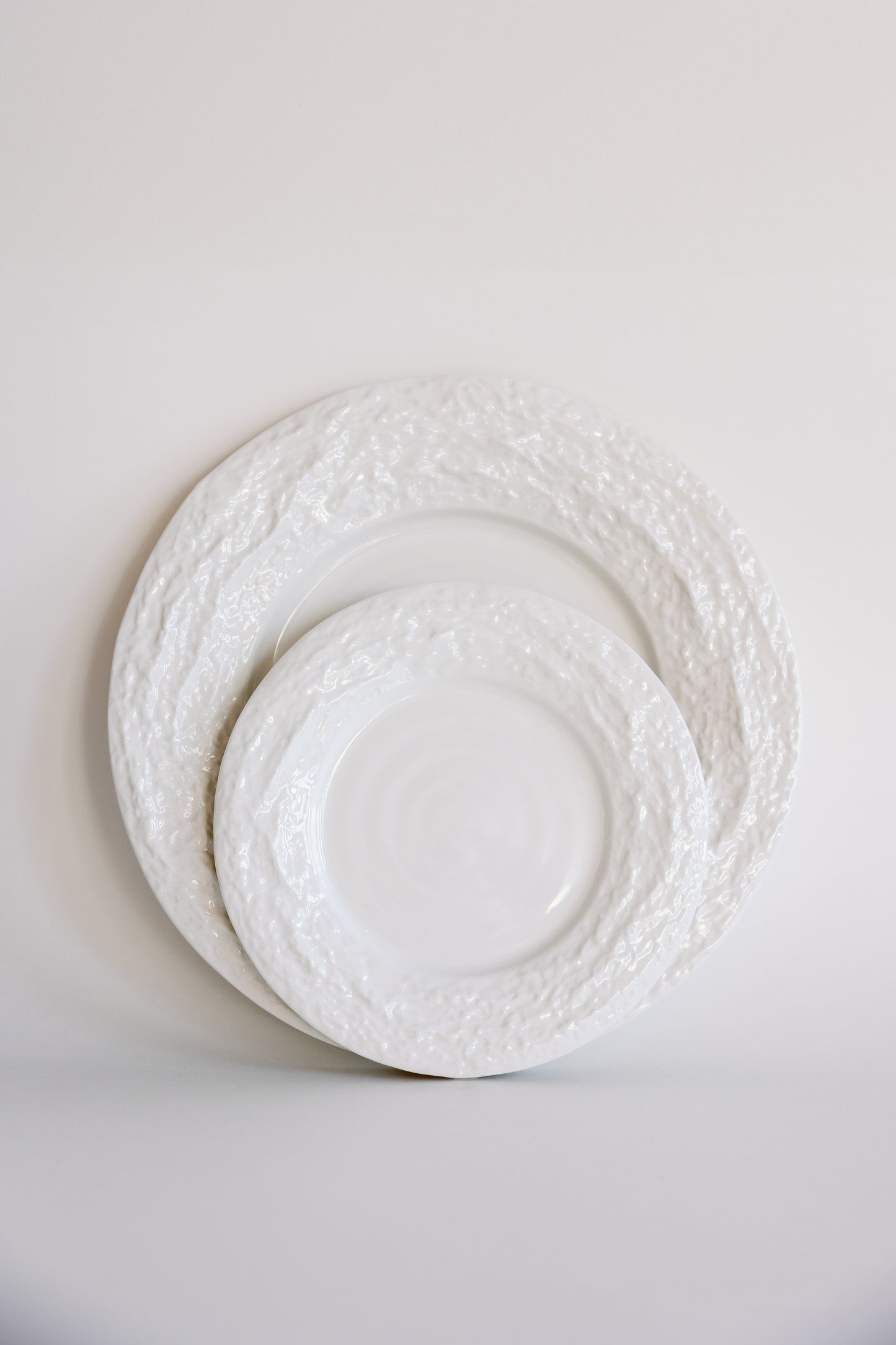 Two white Alpine Snow porcelain plates with rough textured rims stacked in two sizes against a soft white backdrop.