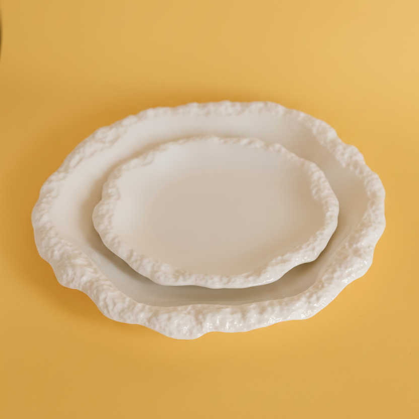 Three nested white ceramic plates with textured, scalloped edges, arranged on a solid mustard yellow background.