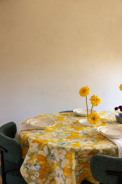 Round table set with Coquette Picnic floral plates, yellow daisies in a vase and green boucle chairs.