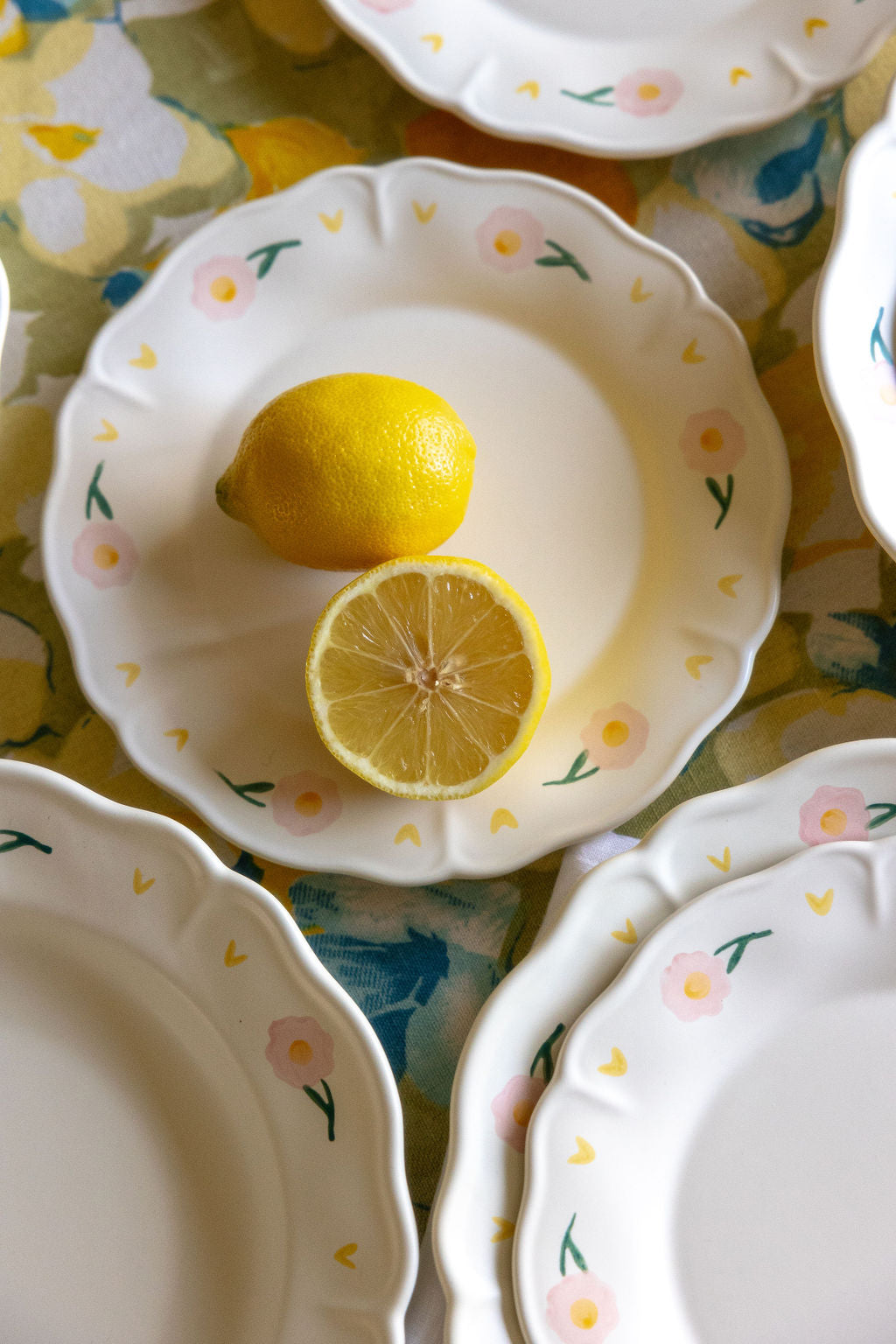 Coquette Picnic porcelain plate with pink floral scalloped rim, styled with whole and halved lemons on floral cloth.