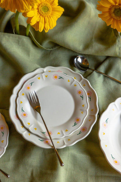 Stacked Coquette Picnic floral plates with a gold fork on a green linen, yellow daisies above.