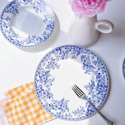 Set of blue floral-patterned plates with a fork, checkered napkin, and pink flower on a white background