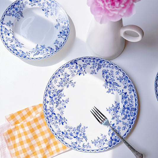 Set of blue floral-patterned plates with a fork, checkered napkin, and pink flower on a white background