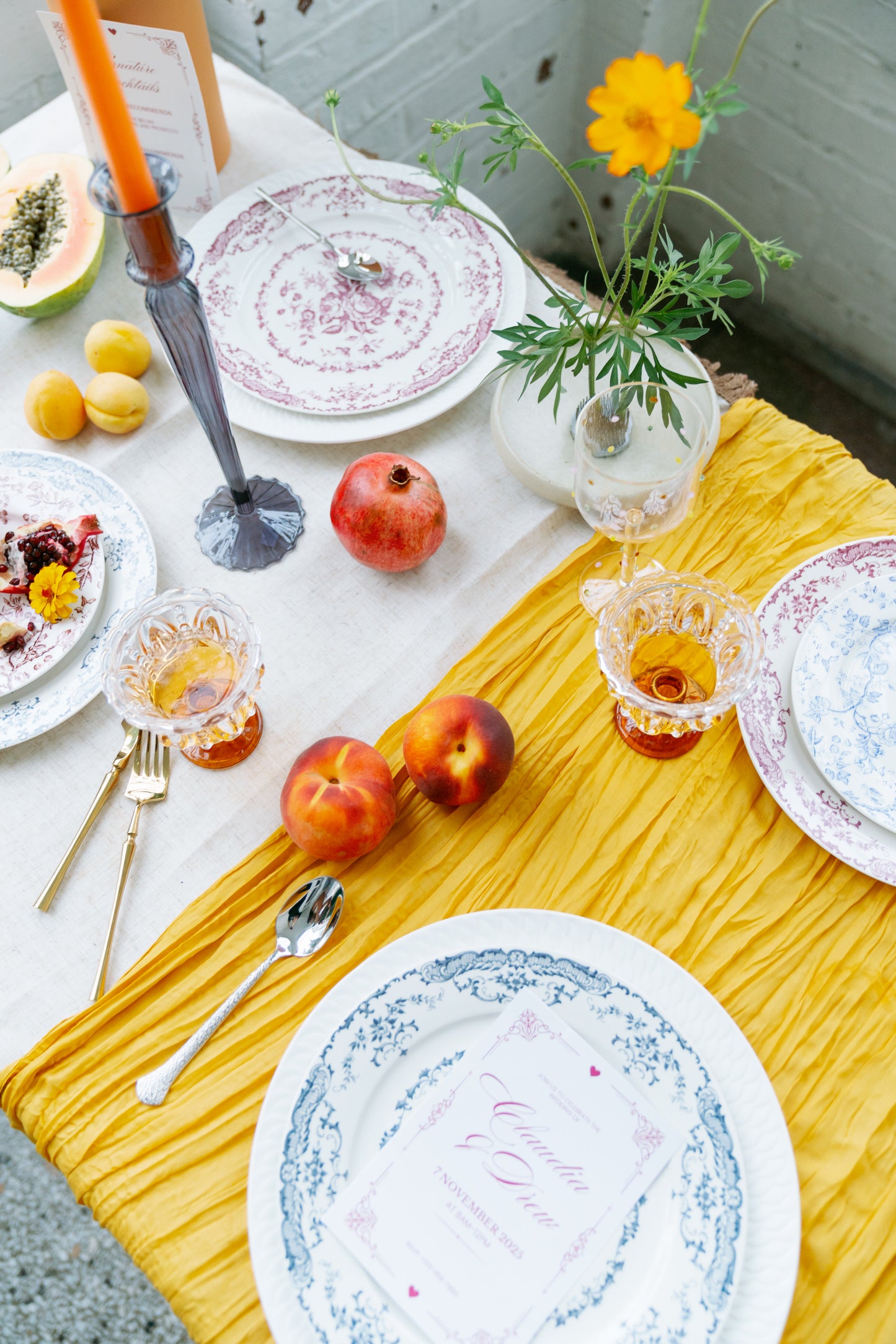 Chantilly Lace plates in red and blue florals set on a mustard runner with fruit and amber glasses, table scene.