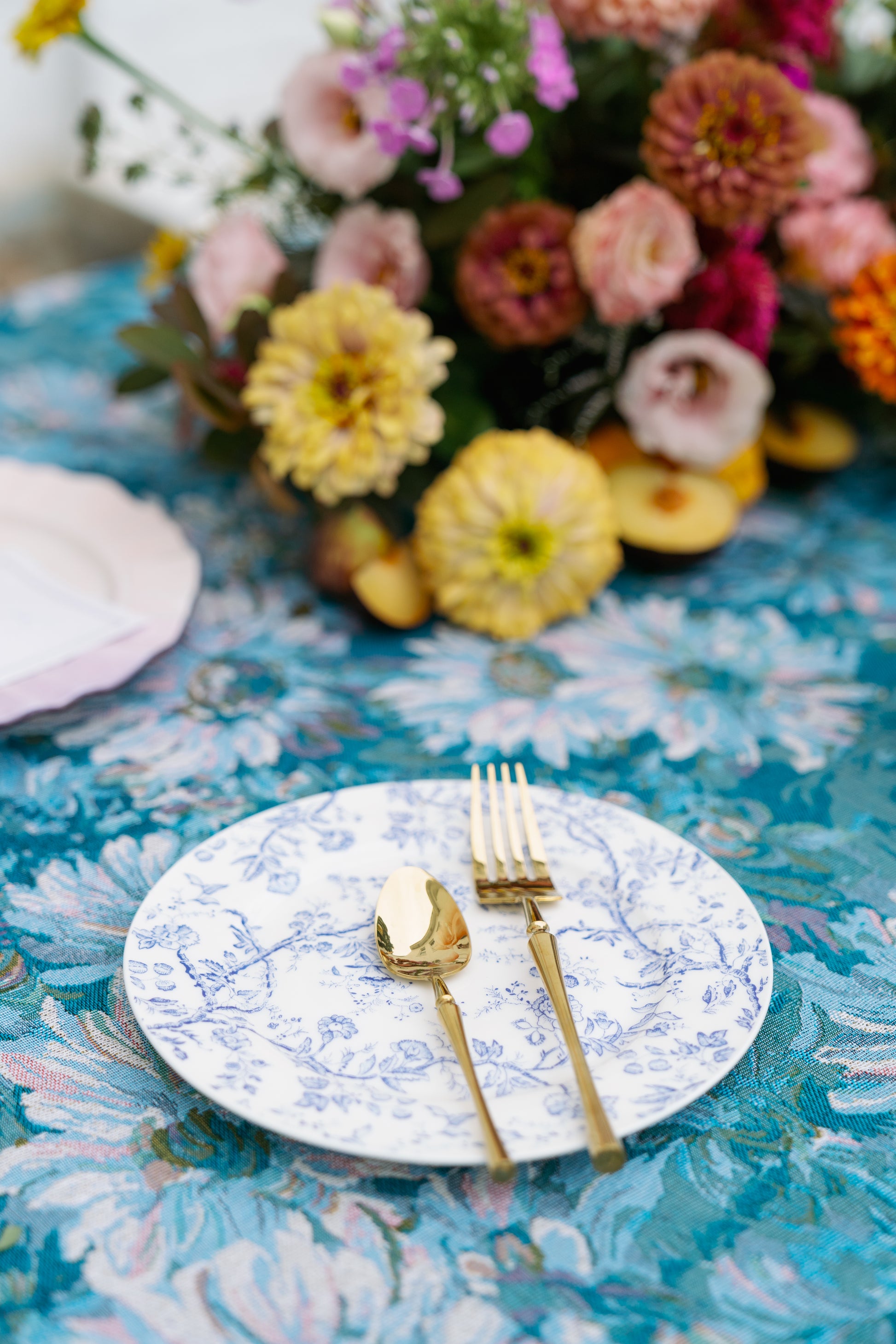 Cottage Garden blue floral plate with gold flatware on a blue floral tablecloth beside a flower bouquet.