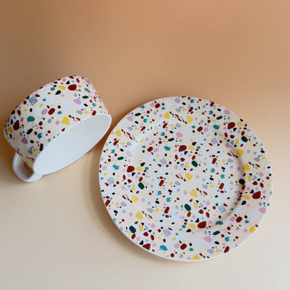 Cup and saucer with multicolored speckled pattern on a beige background