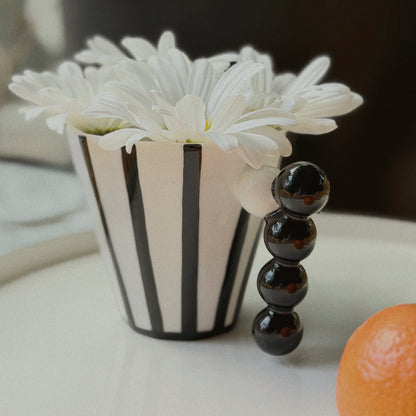 Black and white striped mug with beaded handle with white flowers and an orange on a light surface.