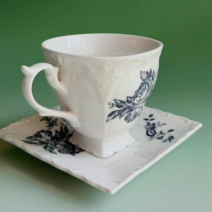 White ceramic cup and saucer with blue floral patterns on a green background