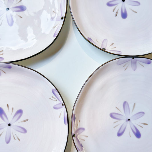 Four ceramic plates with purple floral patterns on a light background