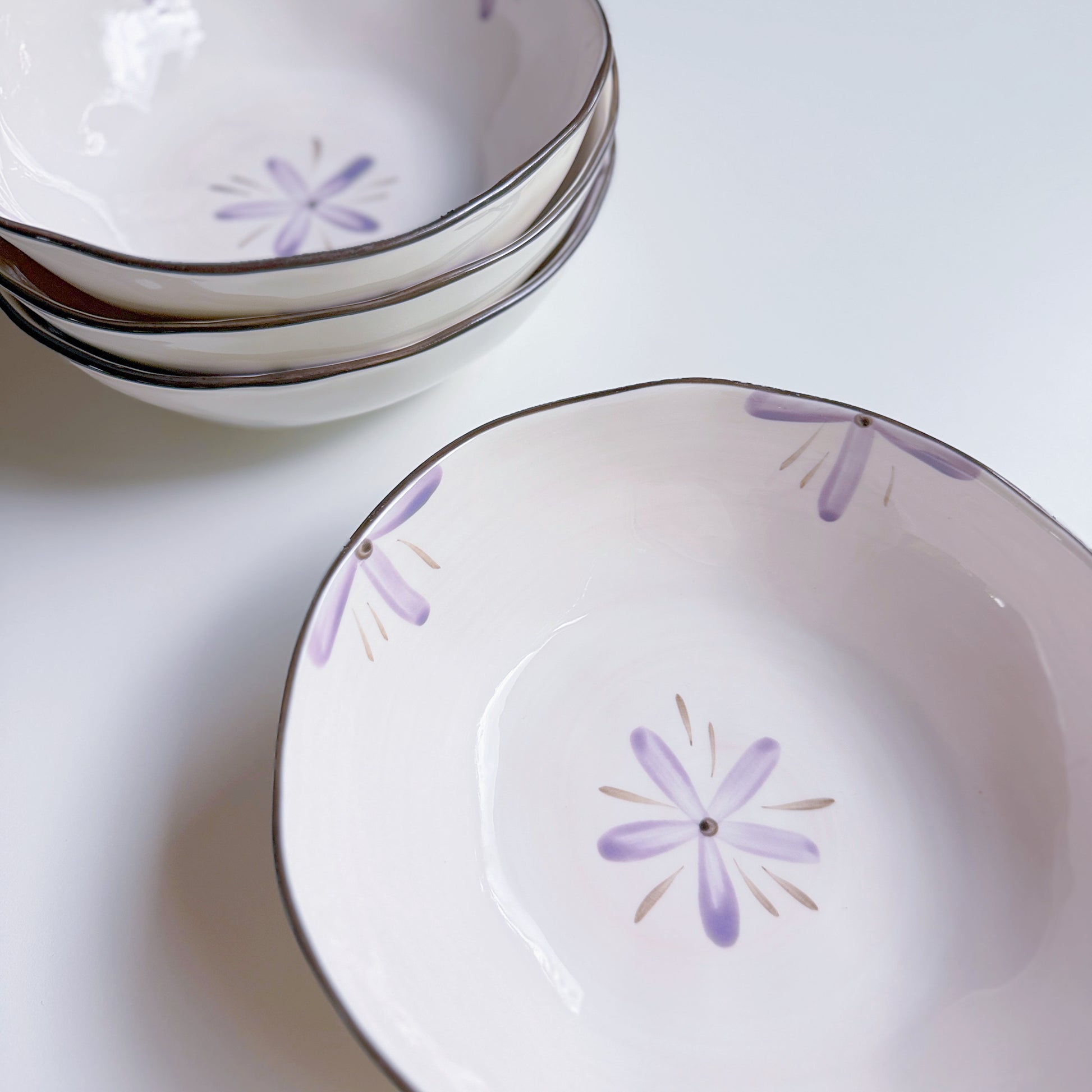 Set of white ceramic bowls with purple floral patterns on a light background