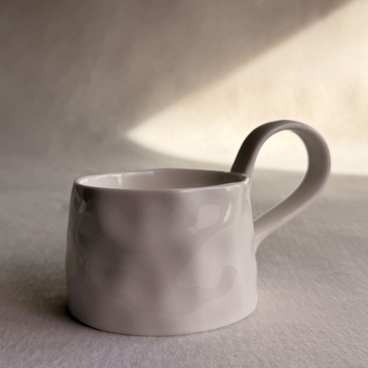 A matte ceramic coffee mug with a unique wavy, organic texture and a curved handle, shown in soft, natural light against a neutral background.
