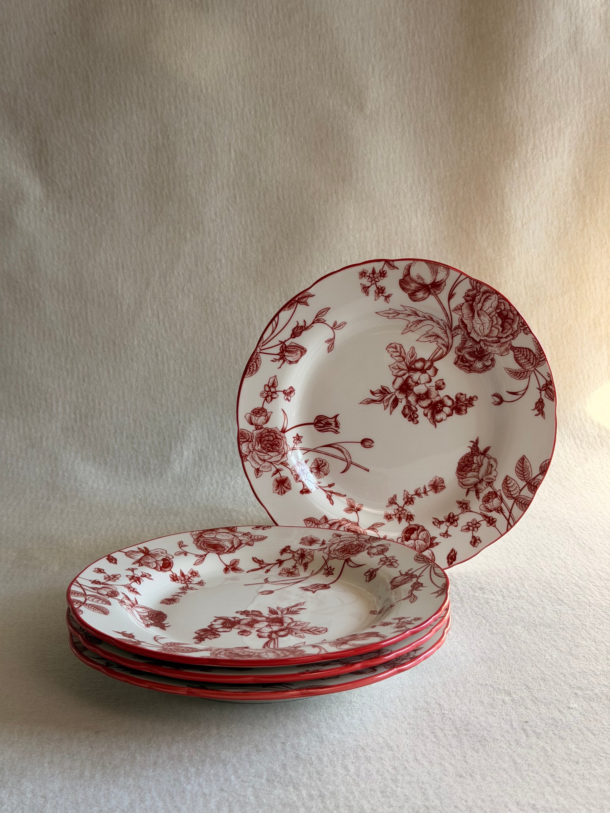 Set of ceramic plates with red floral patterns on a light wooden surface