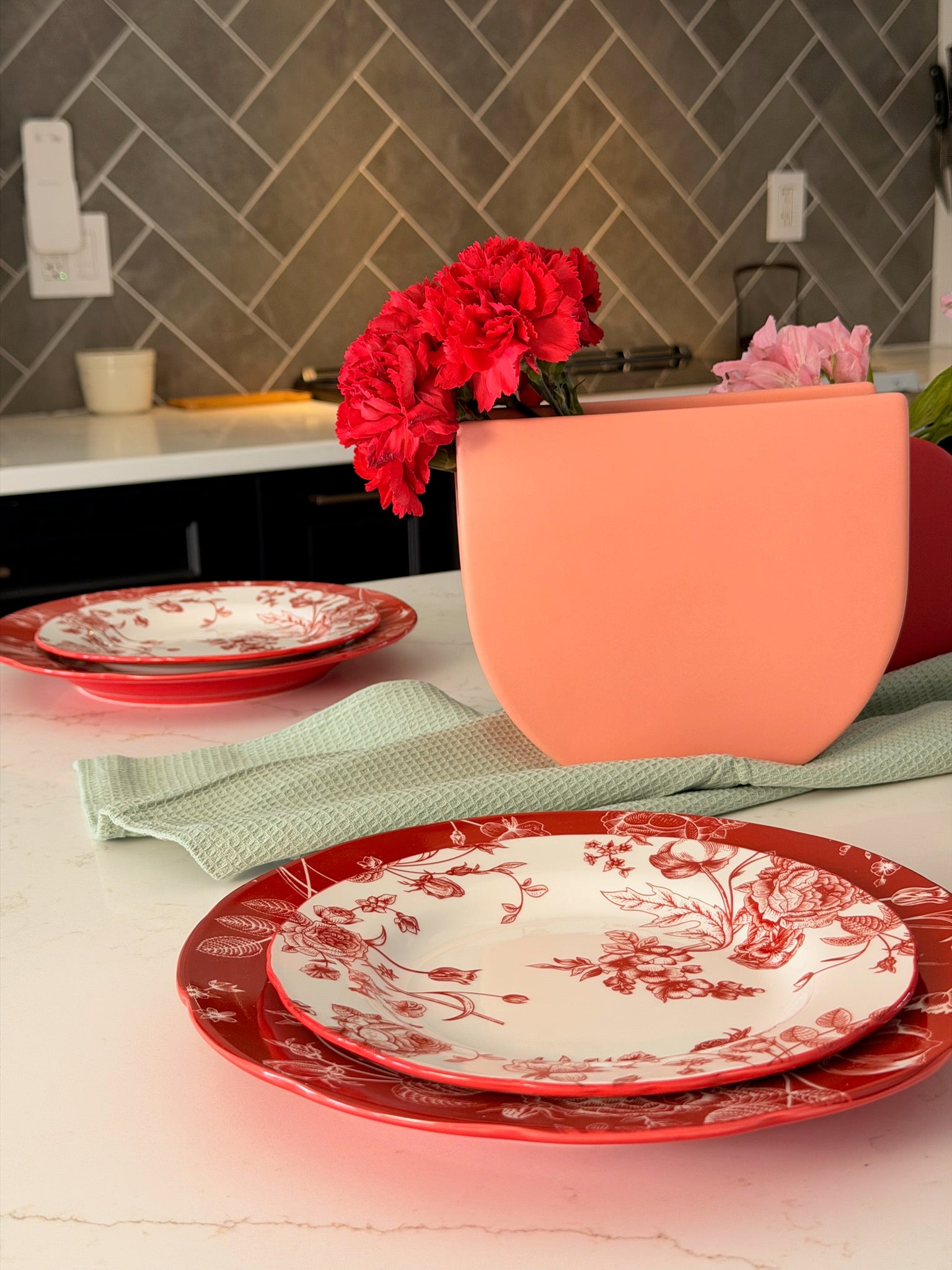 Decorative red and white plates on a kitchen counter with a vase of red flowers.