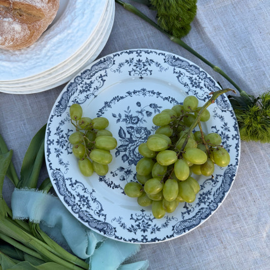 White plate with navy floral pattern with green grapes on a tablecloth with bread and greenery