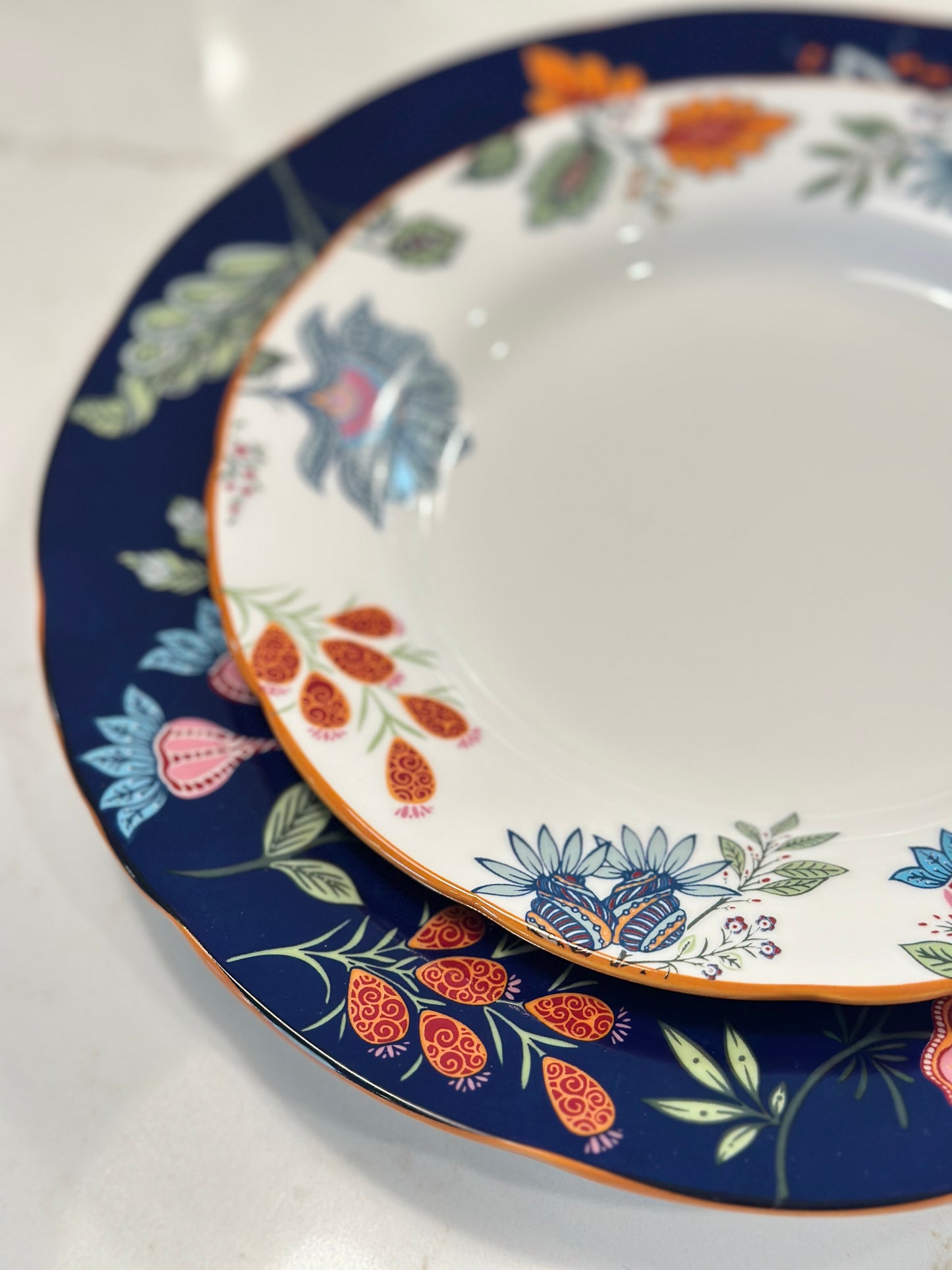 Close-up of Azure Desert floral plates with navy and orange folk flower borders and gold rims, nested in two sizes.