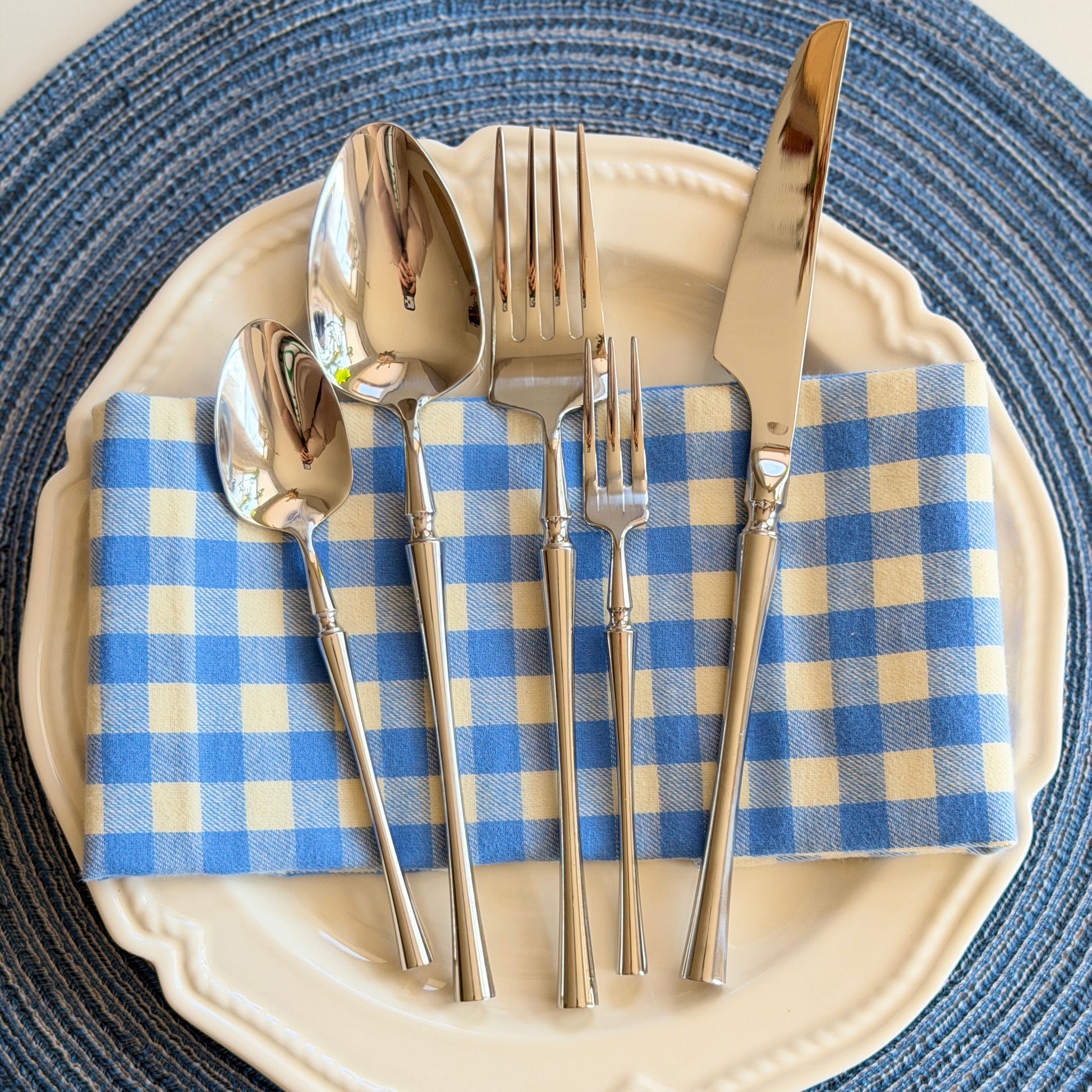Silverware set on a blue and white checkered napkin with a blue woven placemat.
