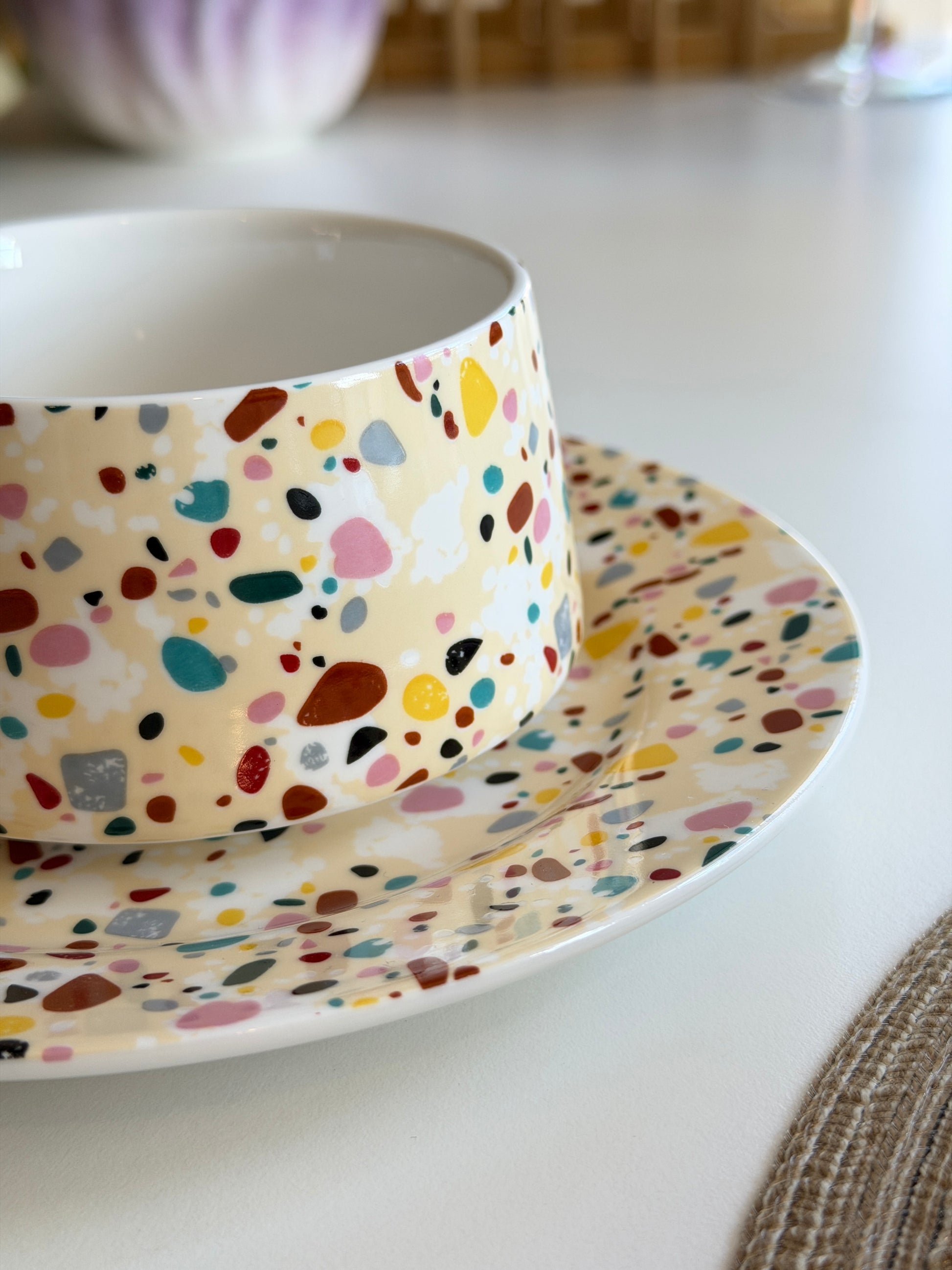 Ceramic tea cup and saucer with multicolored speckled pattern on a white surface