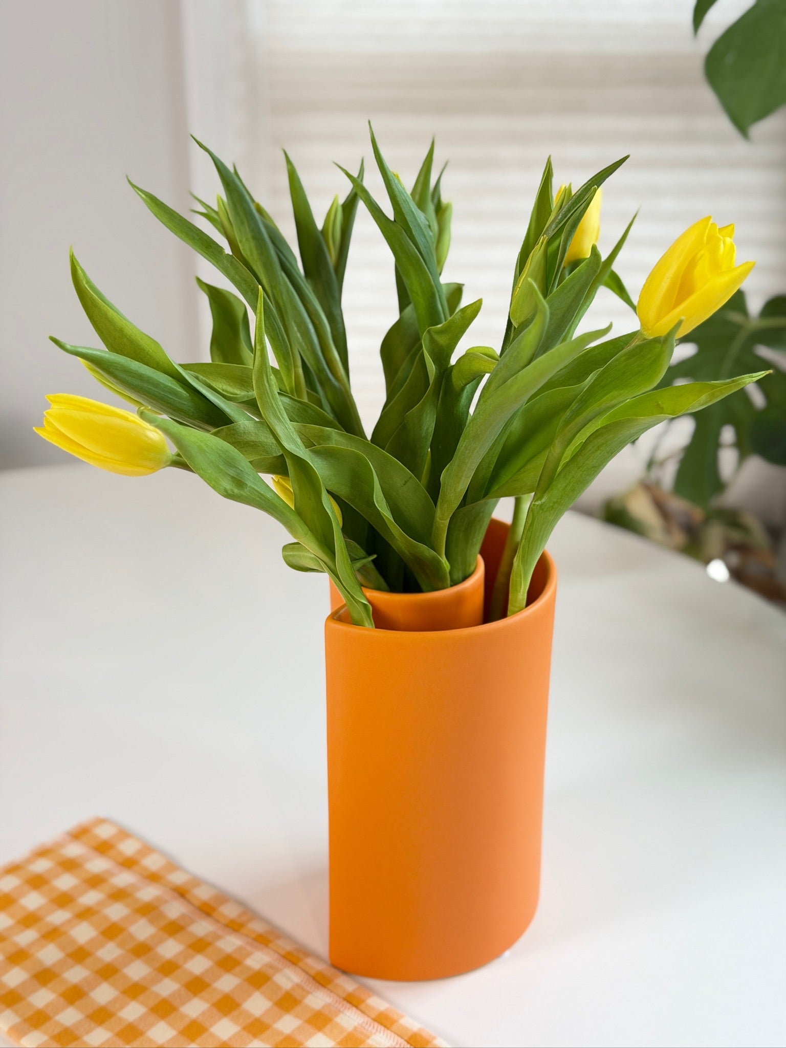 Orange ceramic vase with yellow tulips on a white surface