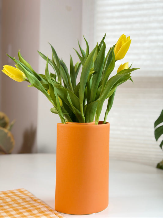 Yellow tulips in an orange vase on a white surface with a blurred background