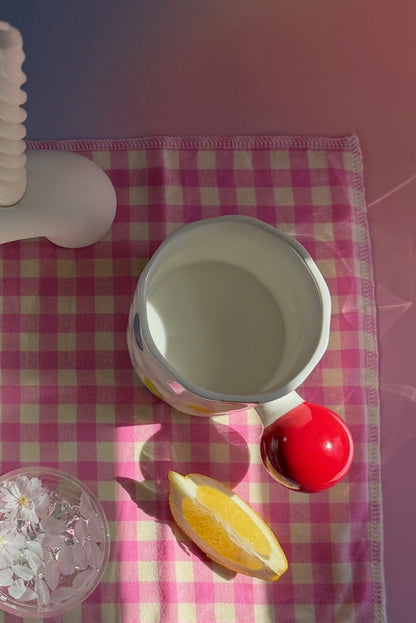 Table setting with teapots, cups, and a banana on a checkered tablecloth.