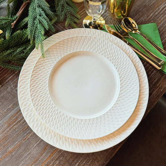 Elegant table setting with white plates, gold cutlery, and candles on a wooden table.