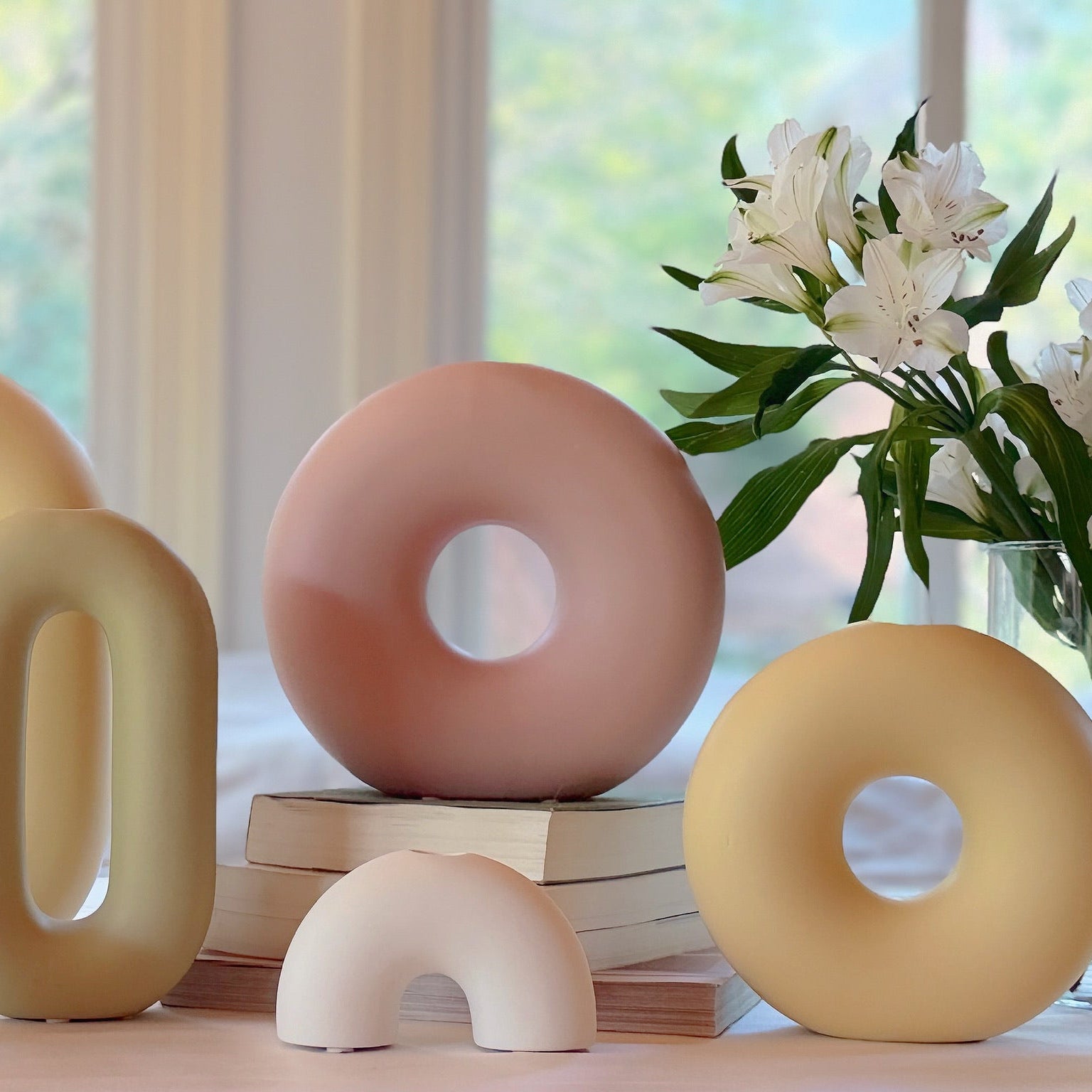 Decorative ceramic donut-shaped objects on a table with a vase of flowers in the background.