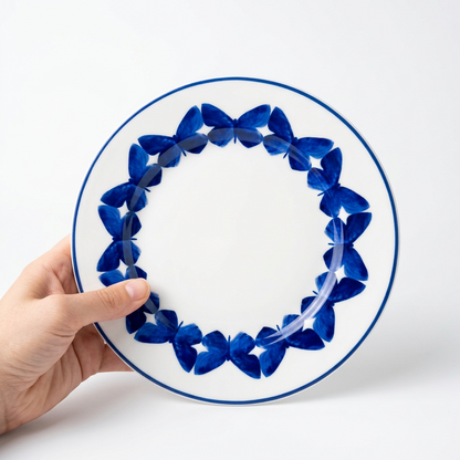 A hand holding a round white ceramic plate with a blue floral border pattern, set against a plain light gray wall.
