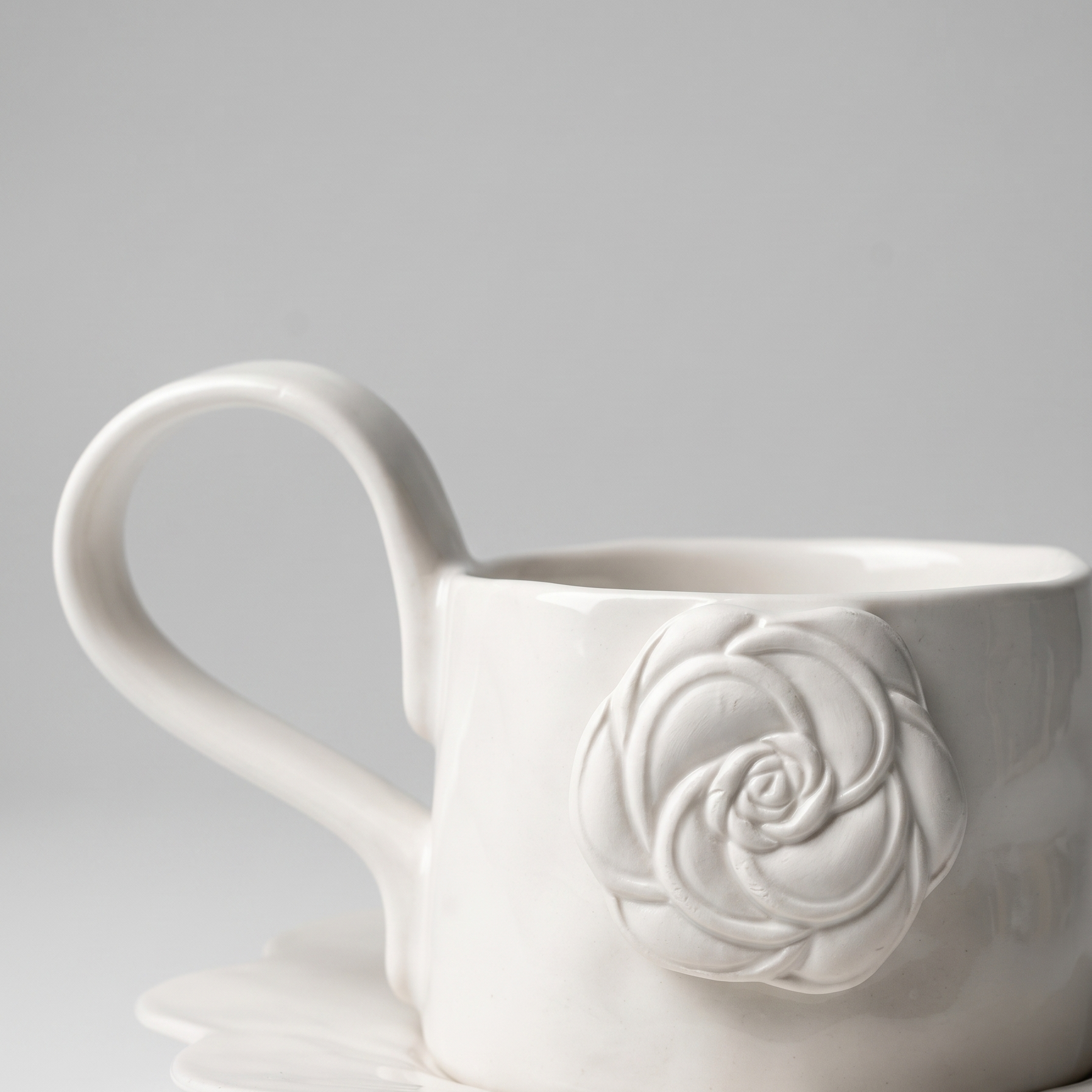white mug with ceramic matte rose detail and long handle on gray background