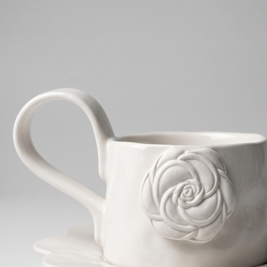 white mug with ceramic matte rose detail and long handle on gray background