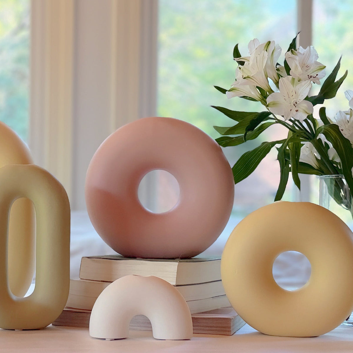 Decorative ceramic donut-shaped objects on a table with a vase of flowers in the background.