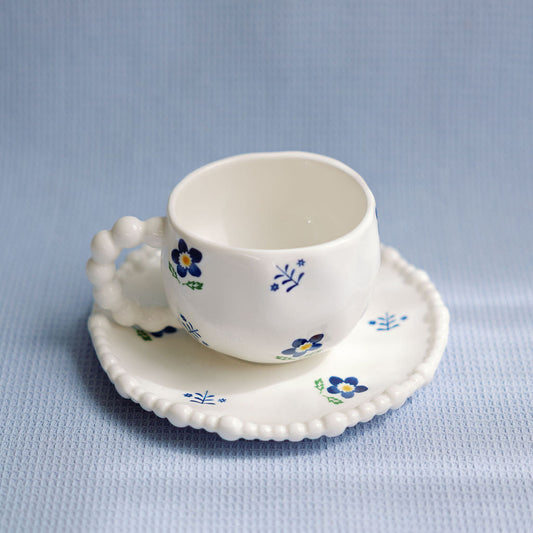 A white ceramic tea cup with blue floral patterns and a saucer with a scalloped edge.