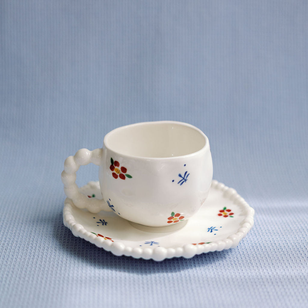 A white ceramic tea cup with blue and red floral patterns and a saucer with a scalloped edge