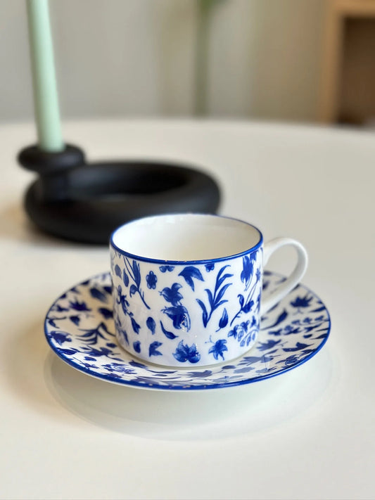 Blue and white floral mug on matching saucer with a green taper candle behind