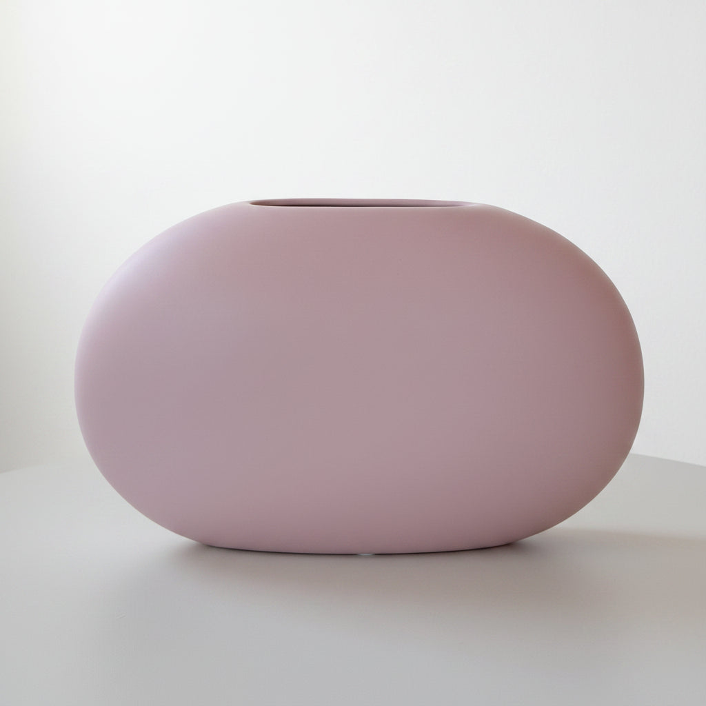 Matte pink oval Blush Stone Ceramic Vase, smooth pebble shape, on a green table against a pale wall.