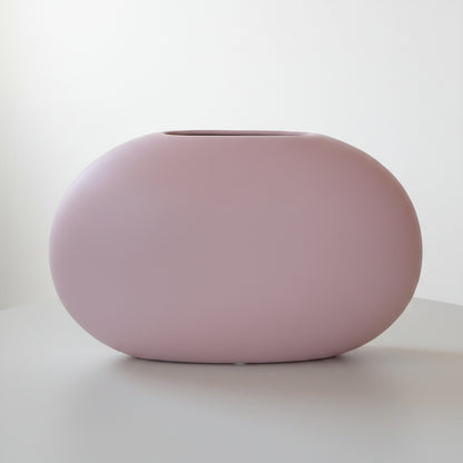 Matte pink oval Blush Stone Ceramic Vase, smooth pebble shape, on a green table against a pale wall.