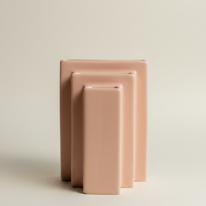 Blush pink bookcase ceramic vase shaped like stacked books in graduated heights, shown against a pale backdrop.