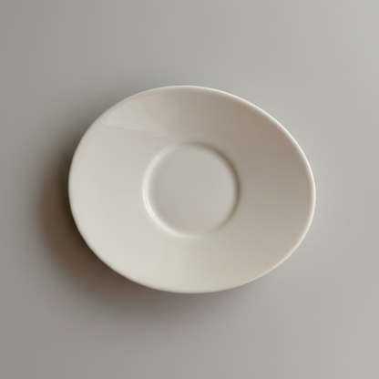 Busy Bee plain white espresso saucer shown from above with its recessed center ring on a beige surface.