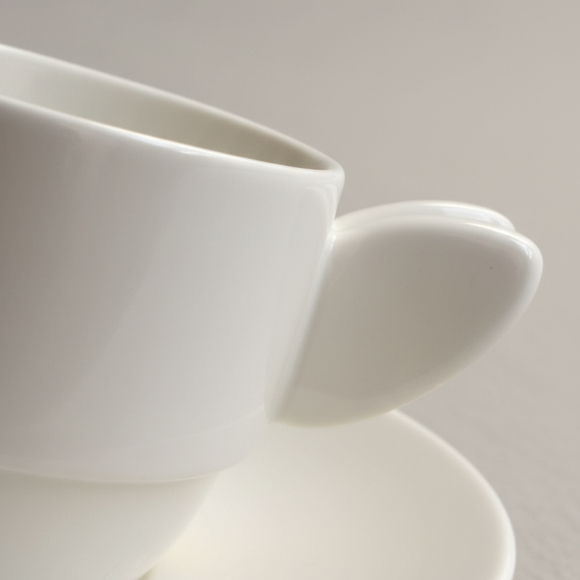 Busy Bee white espresso cup and saucer, close-up of the rim and small handle against a neutral backdrop.