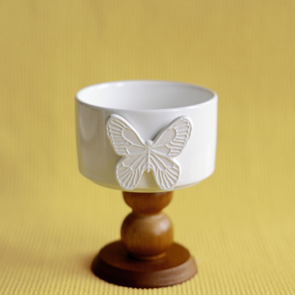 White ceramic cup with butterfly design on a wooden base against a yellow background