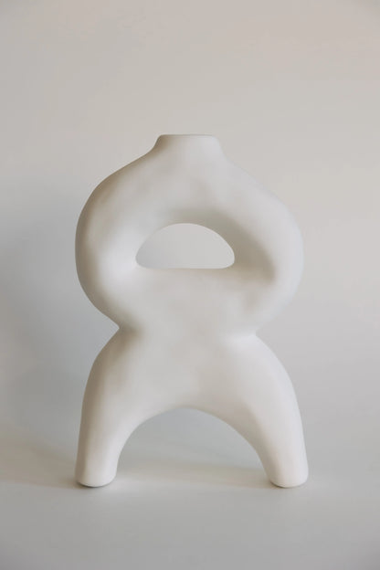 White sculptural bellow bud vase, looped body with arched legs and a triangular cutout, matte ceramic front view