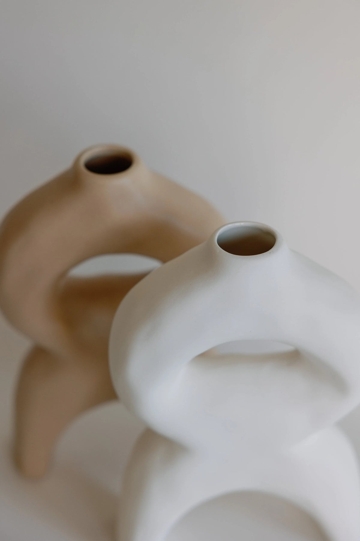 Tan and white bellow bud vases close-up showing the round top openings and looped curves, soft-focus pairing